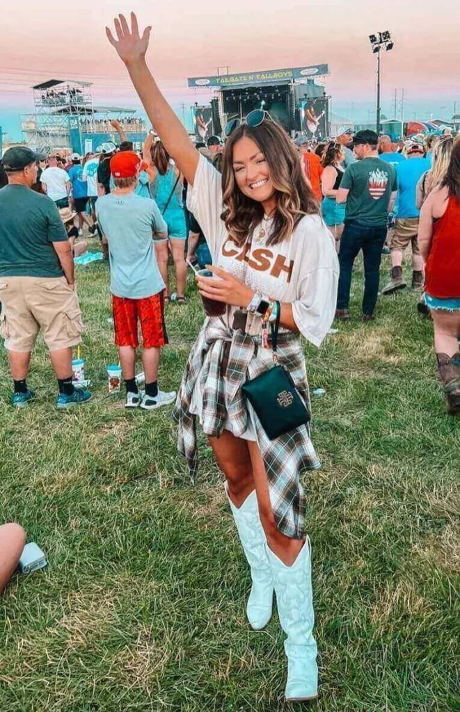 Girl wearing a graphic white shirt with shorts and a flannel around her waist at a country concert