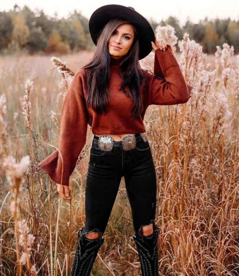 Girl wearing a rust color sweater with dark colored jeans and a hat with black cowboy boots